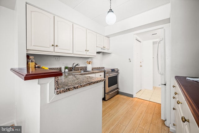 kitchen with stainless steel range with electric cooktop, white cabinetry, dark stone counters, sink, and hanging light fixtures