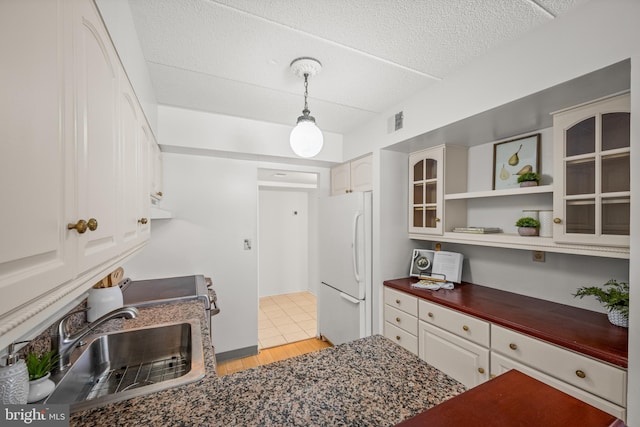 kitchen with white cabinetry, hanging light fixtures, sink, light hardwood / wood-style flooring, and white refrigerator