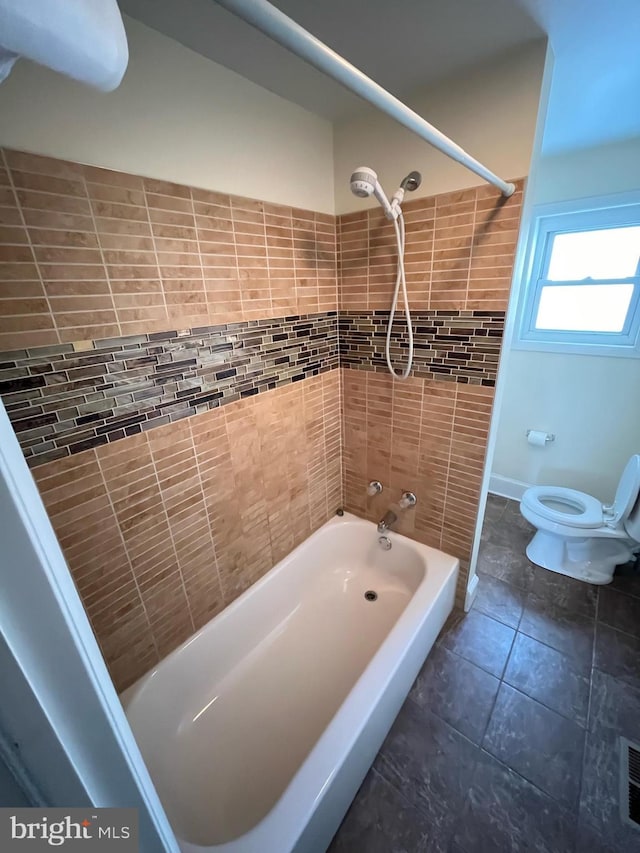 bathroom with tiled shower / bath combo, toilet, and tile patterned floors