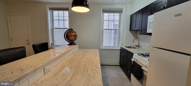 kitchen with a wealth of natural light, sink, decorative backsplash, light stone countertops, and white appliances