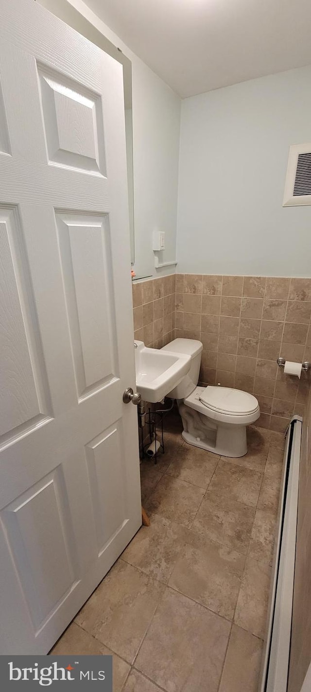 bathroom featuring tile patterned floors, toilet, and tile walls