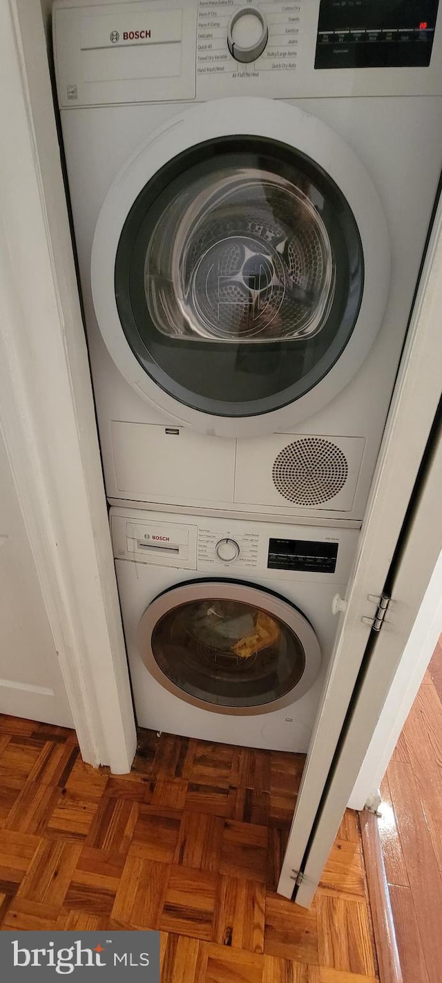 washroom featuring stacked washing maching and dryer and dark parquet floors