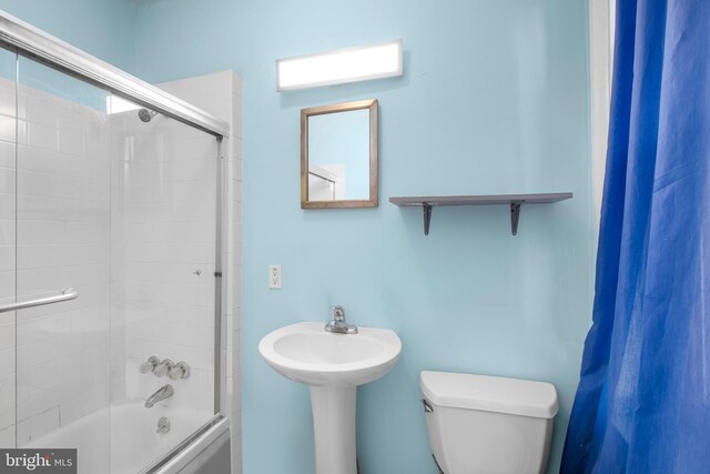 bathroom featuring combined bath / shower with glass door and toilet