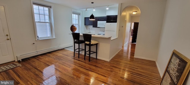 kitchen featuring a kitchen breakfast bar, a baseboard heating unit, kitchen peninsula, dark wood-type flooring, and white appliances