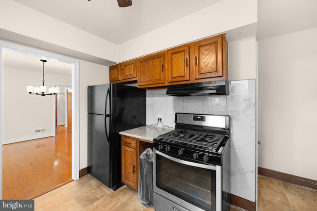 kitchen featuring black refrigerator, hanging light fixtures, tasteful backsplash, ceiling fan with notable chandelier, and gas stove