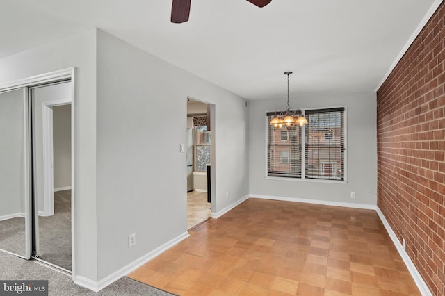 unfurnished dining area with ceiling fan with notable chandelier, brick wall, and parquet floors