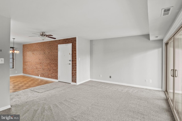 unfurnished living room featuring ceiling fan with notable chandelier, brick wall, and carpet flooring