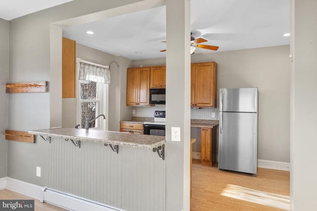 kitchen featuring a breakfast bar, light hardwood / wood-style floors, black appliances, a baseboard radiator, and kitchen peninsula