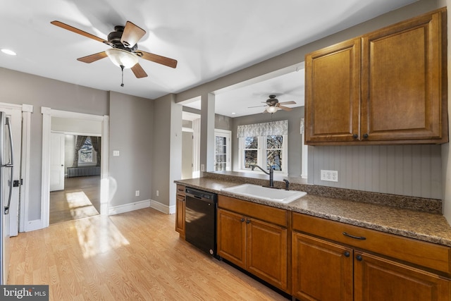 kitchen with sink, radiator, stainless steel refrigerator, black dishwasher, and light wood-type flooring