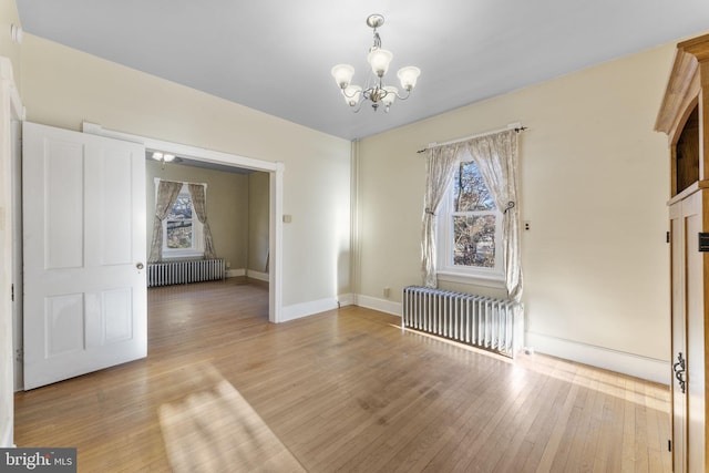 spare room featuring radiator, a chandelier, and light wood-type flooring