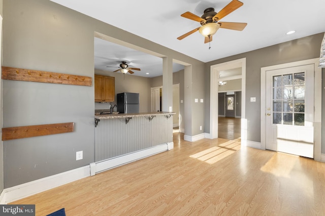 kitchen with a breakfast bar, refrigerator, baseboard heating, light hardwood / wood-style floors, and kitchen peninsula