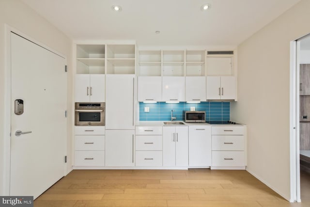 kitchen featuring white cabinets, stainless steel appliances, decorative backsplash, sink, and light hardwood / wood-style floors