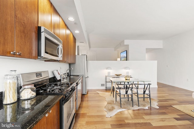 kitchen with appliances with stainless steel finishes, sink, dark stone counters, and light wood-type flooring