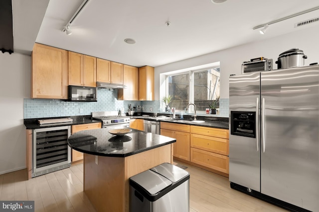 kitchen with beverage cooler, appliances with stainless steel finishes, a kitchen island, light brown cabinets, and sink