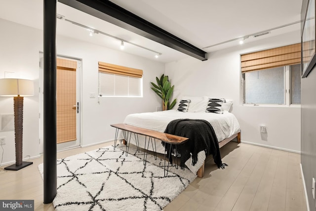 bedroom with rail lighting, light hardwood / wood-style flooring, and beam ceiling