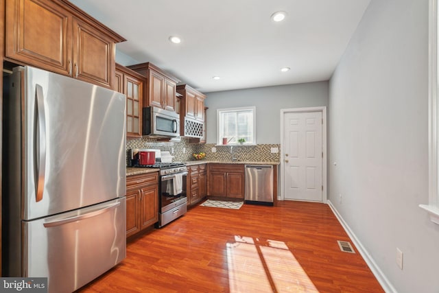 kitchen with hardwood / wood-style flooring, light stone countertops, decorative backsplash, and stainless steel appliances