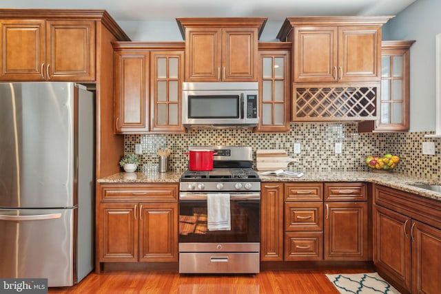 kitchen with light hardwood / wood-style floors, decorative backsplash, light stone countertops, and appliances with stainless steel finishes