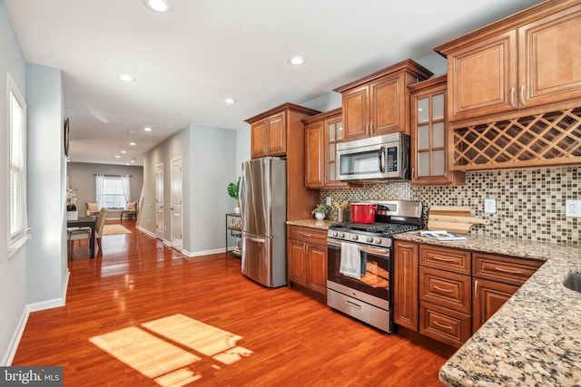 kitchen featuring backsplash, light stone counters, appliances with stainless steel finishes, and wood-type flooring