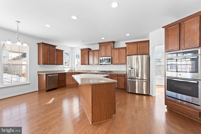 kitchen featuring light stone counters, a center island, hanging light fixtures, stainless steel appliances, and hardwood / wood-style floors