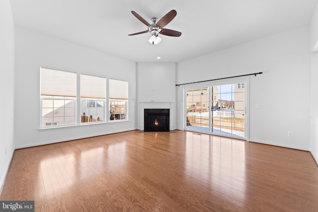 unfurnished living room featuring wood-type flooring, plenty of natural light, and ceiling fan