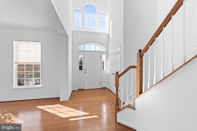 foyer with crown molding, a high ceiling, and light wood-type flooring