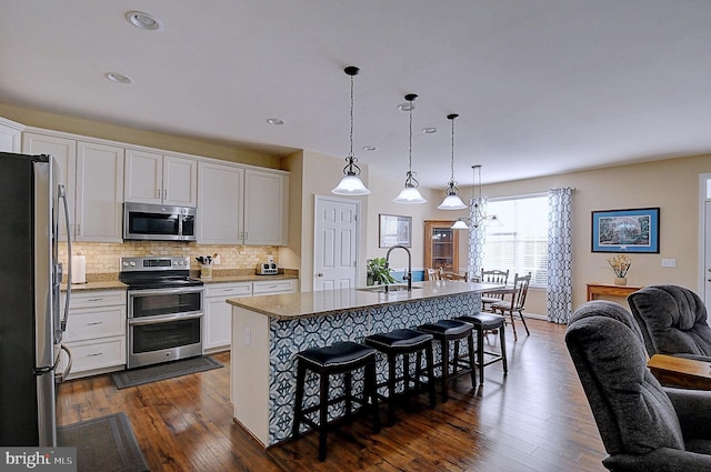 kitchen featuring a kitchen bar, sink, white cabinetry, appliances with stainless steel finishes, and a kitchen island with sink