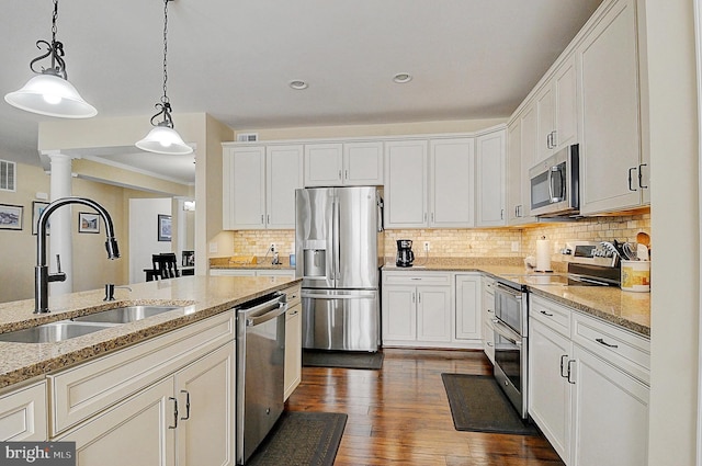 kitchen with appliances with stainless steel finishes, pendant lighting, sink, white cabinets, and light stone counters