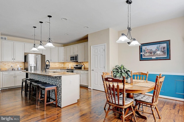 kitchen featuring appliances with stainless steel finishes, pendant lighting, sink, white cabinets, and a center island with sink