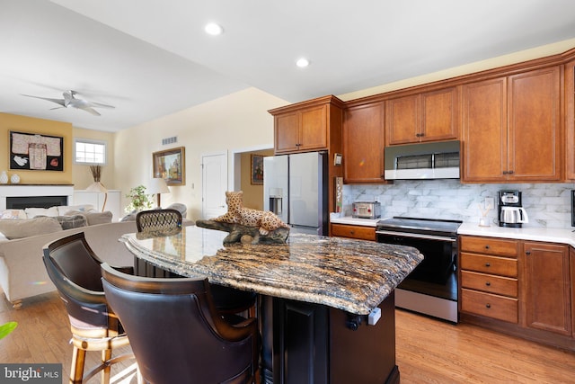 kitchen with backsplash, appliances with stainless steel finishes, a center island, and light hardwood / wood-style flooring