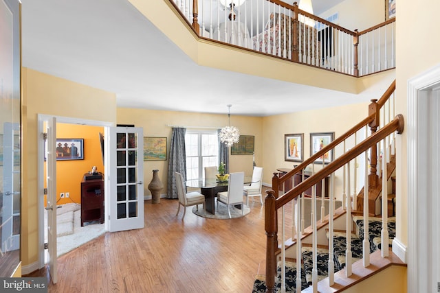 staircase featuring a chandelier, a towering ceiling, french doors, and wood-type flooring