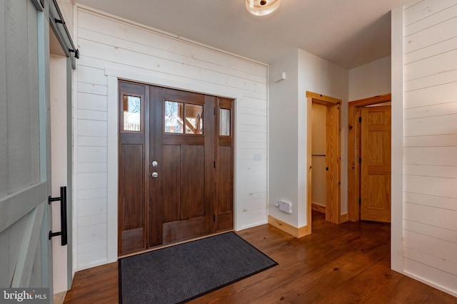 entrance foyer with a barn door, dark hardwood / wood-style flooring, and wood walls