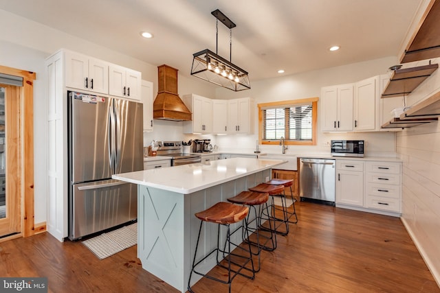 kitchen with custom exhaust hood, appliances with stainless steel finishes, a kitchen island, pendant lighting, and white cabinets