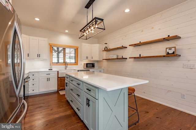 kitchen featuring wood walls, white cabinetry, hanging light fixtures, a kitchen island, and stainless steel appliances