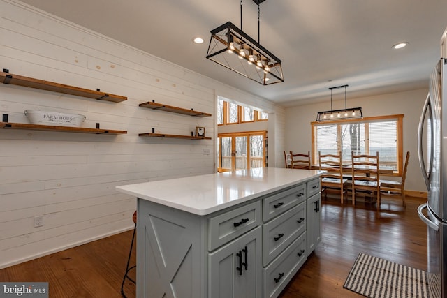 kitchen featuring dark wood-type flooring, decorative light fixtures, stainless steel refrigerator, wooden walls, and a kitchen island