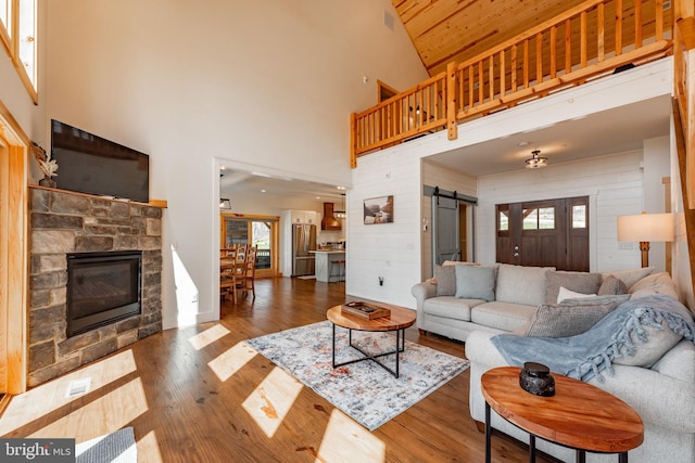 living room featuring a barn door, wood-type flooring, wooden walls, and high vaulted ceiling