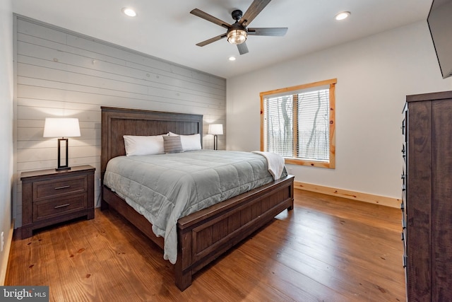 bedroom with light hardwood / wood-style flooring, ceiling fan, and wood walls