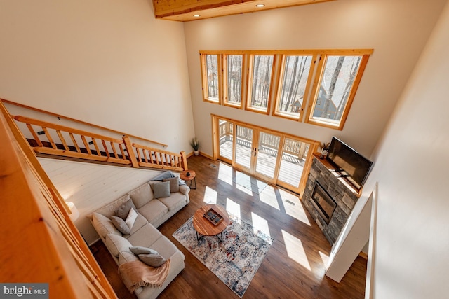 living room with a towering ceiling, a stone fireplace, french doors, and hardwood / wood-style flooring