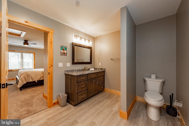 bathroom featuring ceiling fan, hardwood / wood-style floors, a skylight, vanity, and toilet