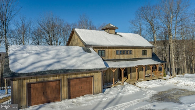 snow covered property featuring a porch and a garage