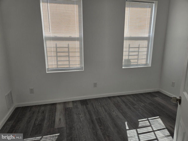 empty room featuring a healthy amount of sunlight, dark wood-style floors, visible vents, and baseboards