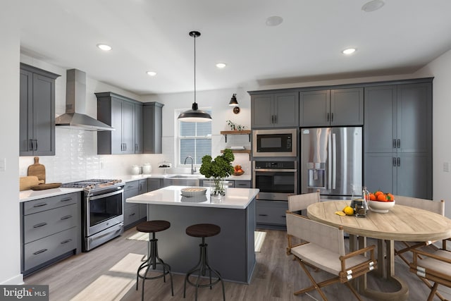 kitchen featuring pendant lighting, appliances with stainless steel finishes, gray cabinetry, and wall chimney exhaust hood