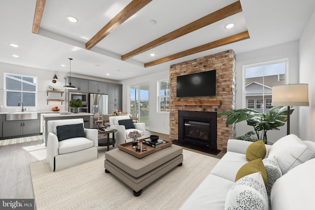 living room with sink, light hardwood / wood-style floors, beam ceiling, and a stone fireplace