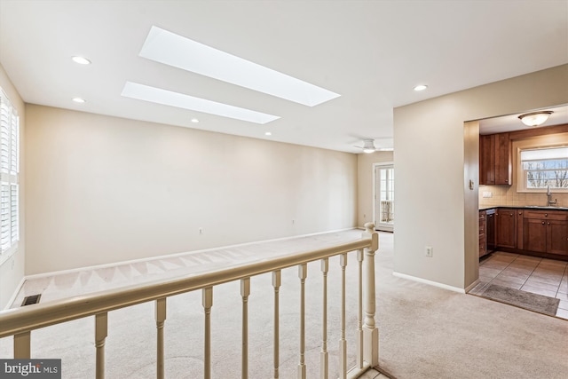 hallway featuring light carpet, a skylight, baseboards, a sink, and recessed lighting