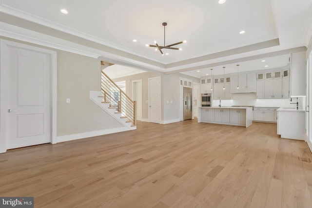 unfurnished living room with an inviting chandelier, light hardwood / wood-style flooring, a raised ceiling, and ornamental molding