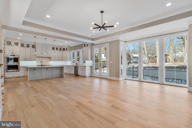 unfurnished living room with crown molding, light hardwood / wood-style flooring, sink, a tray ceiling, and a notable chandelier