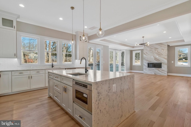 kitchen featuring a high end fireplace, light stone countertops, sink, pendant lighting, and an island with sink