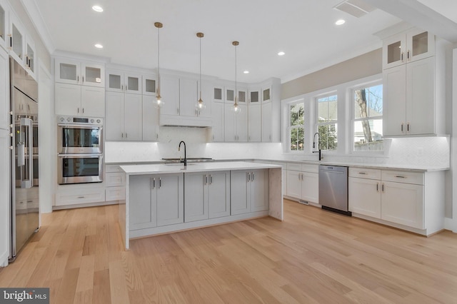 kitchen with white cabinets, a kitchen island with sink, appliances with stainless steel finishes, and pendant lighting