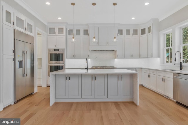 kitchen with pendant lighting, appliances with stainless steel finishes, white cabinetry, sink, and a kitchen island with sink