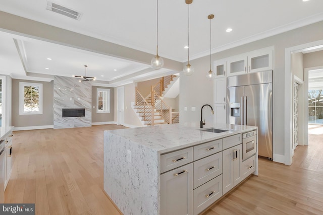 kitchen with built in appliances, hanging light fixtures, a kitchen island with sink, sink, and white cabinets