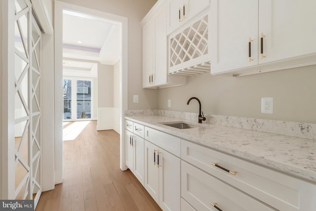 kitchen with sink, light wood-type flooring, white cabinets, and light stone countertops